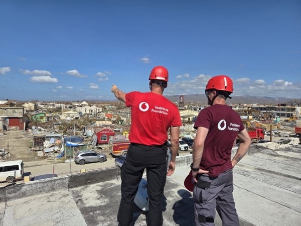 two men stand on rooftop and look over destroyed town